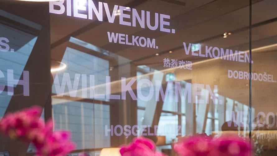 Welcome in several languages behind pink flower arrangement