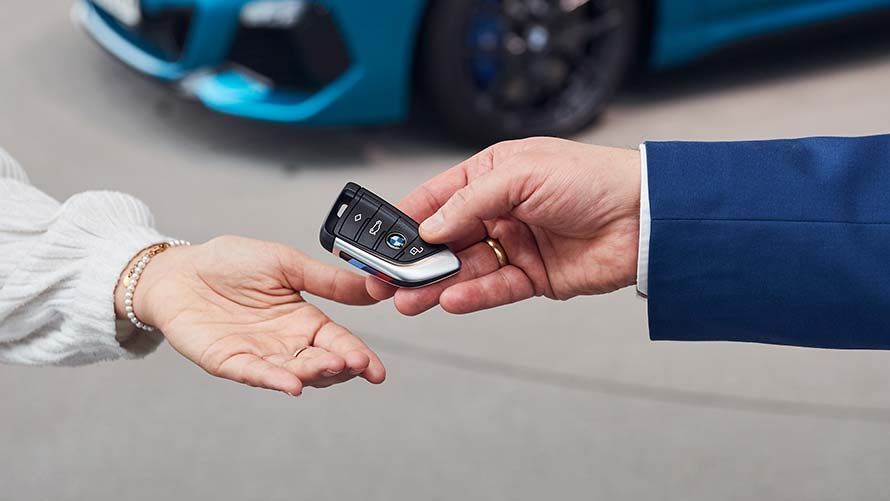 Handing over the keys in front of a metallic blue BMW model at BMW Welt
