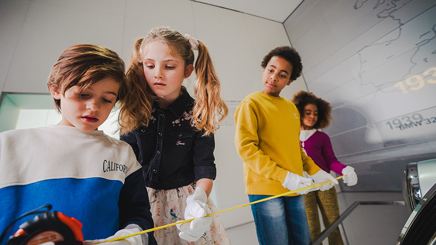 Kinder vermessen Fahrzeuge im BMW Museum, um Hinweise zu finden