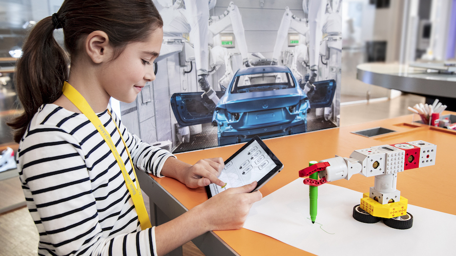 Girl controls a small Lego robot with the help of a tablet